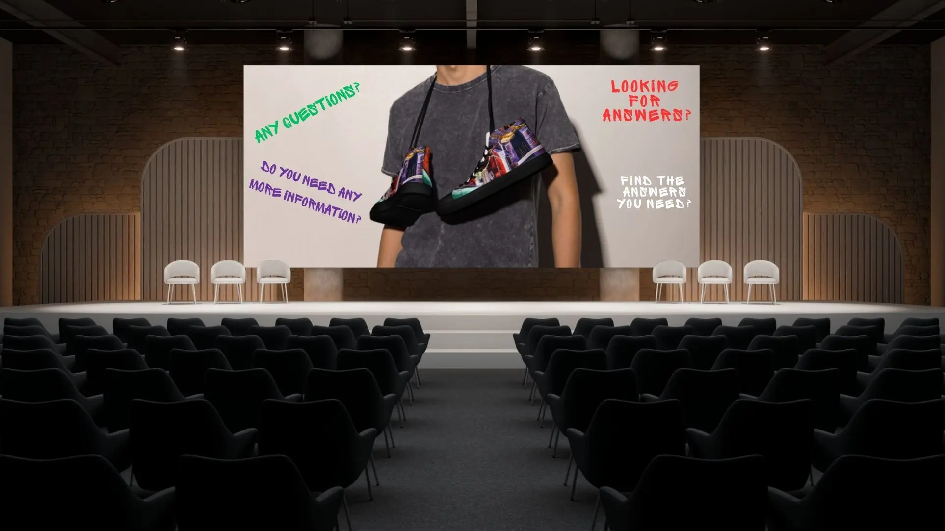 A modern auditorium with rows of black chairs facing a large stage, where a screen displays a person wearing a faded black t-shirt with a pair of colourful high-top canvas shoes with Paul Corps City Lane Design draped around their neck. The screen features graffiti-style text in green, purple, red, and white asking, "Any questions?", "Do you need any more information?", "Looking for answers?", and "Find the answers you need?"