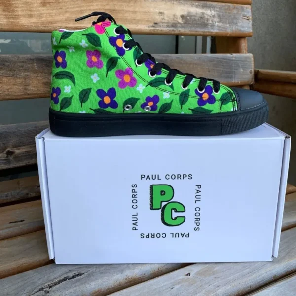 A pair of vibrant green high-top canvas shoes with a colorful floral pattern, black laces, and black soles, displayed on top of a white box labeled "Paul Corps."