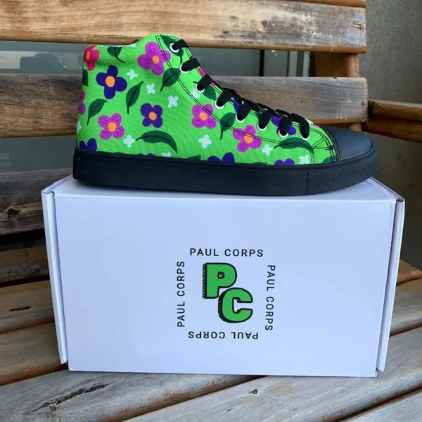 A pair of vibrant green high-top canvas shoes with a colorful floral pattern, black laces, and black soles, displayed on top of a white box labeled "Paul Corps."