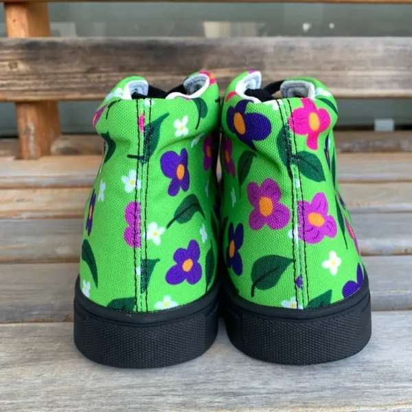 A pair of vibrant Paul Corps green high-top canvas shoes with a colorful floral pattern, black laces, and black soles, facing the heel