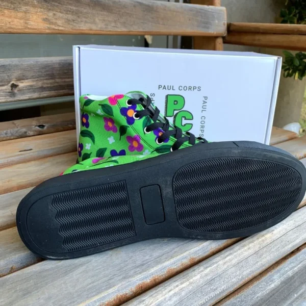 A pair of vibrant green high-top canvas shoes with a colorful floral pattern, black laces, and black soles, displayed in front of a white box labeled "Paul Corps." One laying on it's side showing the sole.