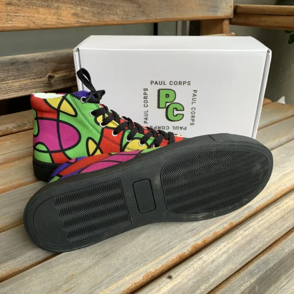 Side view of Paul Corps Lava Lamp Memories high-top canvas shoes, showing the colorful abstract design and black sole, with one shoe on its side displaying the sole, next to a white Paul Corps branded box on a wooden bench.