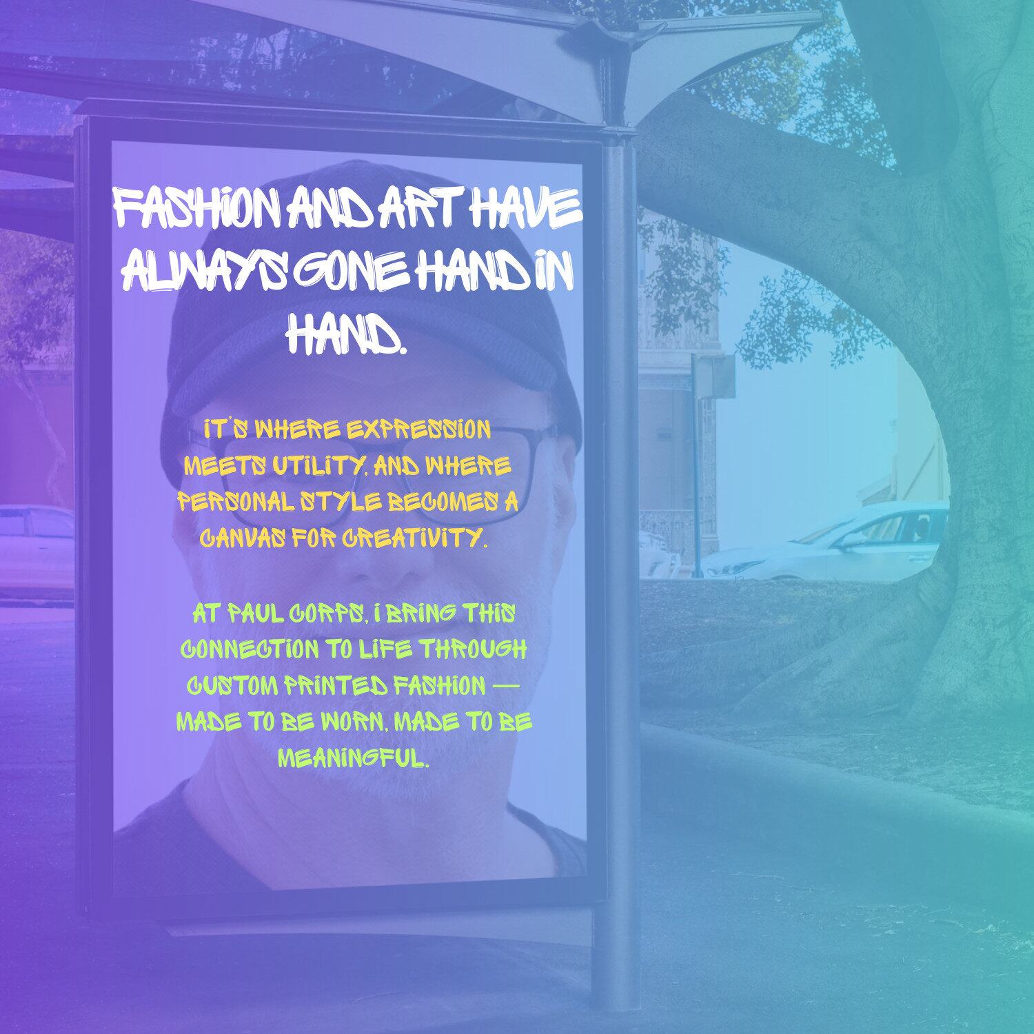 A bus stop advertisement featuring a portrait of Paul Corps with overlay text in bold white and yellow graffiti-style fonts, reading: "Fashion and art have always gone hand in hand. It’s where expression meets utility, and where personal style becomes a canvas for creativity. At Paul Corps, I bring this connection to life through custom printed fashion—made to be worn. Made to be meaningful." The background shows trees, a street, and parked cars.