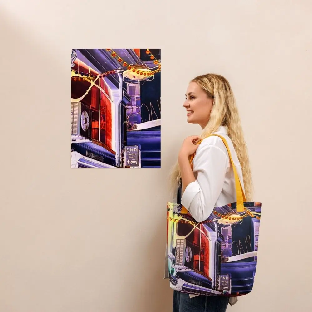 A Paul Corps tote bag featuring a vibrant, digitally enhanced photograph of a Melbourne laneway. The design includes colorful string lights, urban signage, and architectural details in shades of purple, orange, and blue, with black handles.