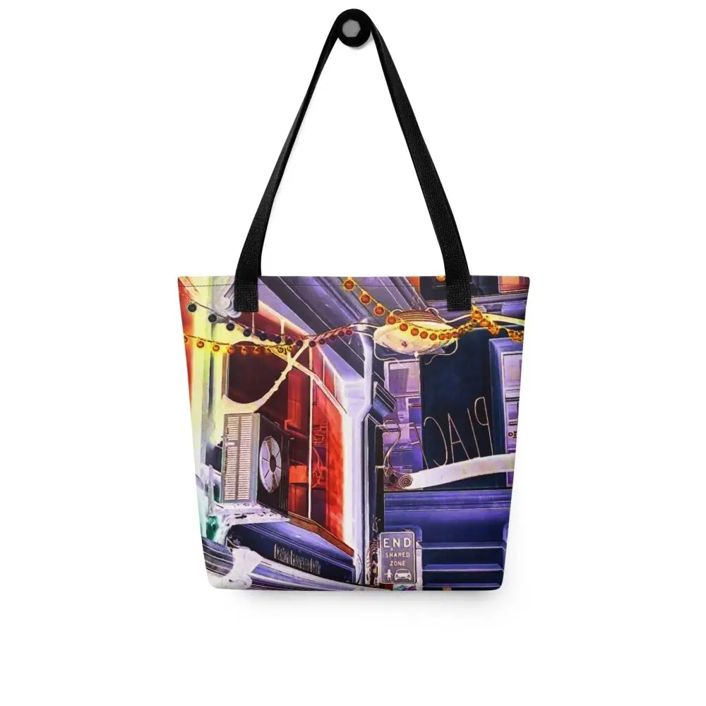 A Paul Corps tote bag featuring a vibrant, digitally enhanced photograph of a Melbourne laneway. The design includes colorful string lights, urban signage, and architectural details in shades of purple, orange, and blue, with black handles.