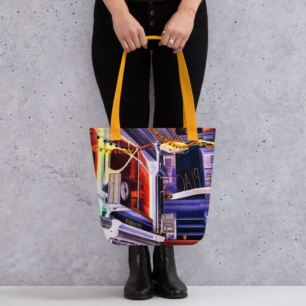 A Paul Corps tote bag featuring a vibrant, digitally enhanced photograph of a Melbourne laneway. The design includes colorful string lights, urban signage, and architectural details in shades of purple, orange, and blue, with black handles.