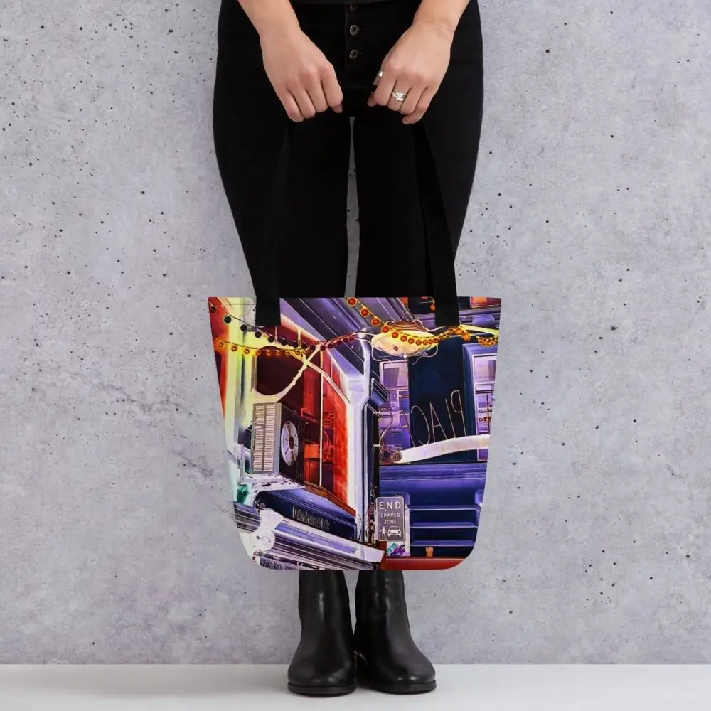 A Paul Corps tote bag featuring a vibrant, digitally enhanced photograph of a Melbourne laneway. The design includes colorful string lights, urban signage, and architectural details in shades of purple, orange, and blue, with black handles.