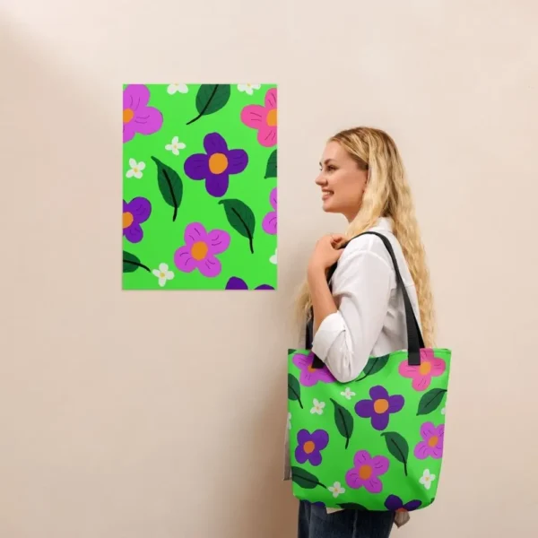A person wearing a Green Spring all-over print tote bag with black handles over their shoulder, standing in front of a matching an art print on a beige wall