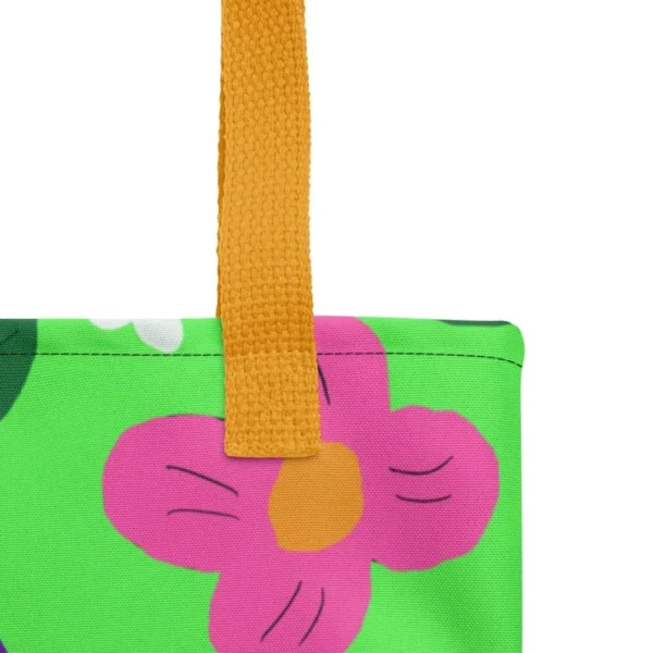 Close-up of the top corner of a Green Spring all-over print tote bag, showing the yellow handle and detailed stitching with the colourful flower and leaf in pink, yellow, white and purple