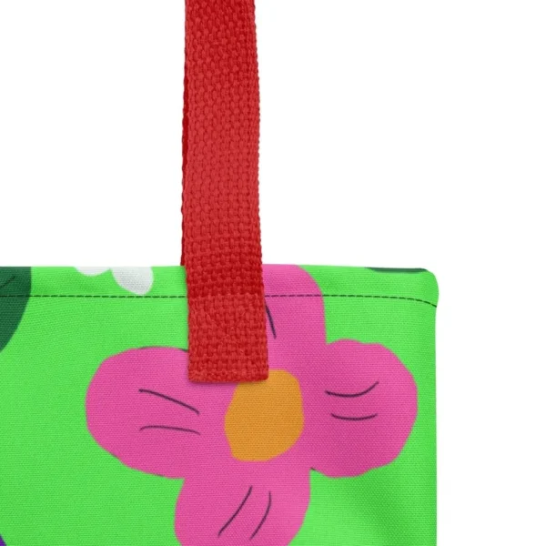 Close-up of the top corner of a Green Spring all-over print tote bag, showing the red handle and detailed stitching with the colourful flower and leaf in pink, yellow, white and purple