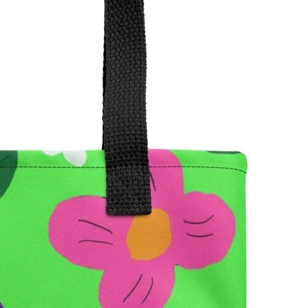 Close-up of the top corner of a Green Spring all-over print tote bag, showing the black handle and detailed stitching with the colourful flower and leaf in pink, yellow, white and purple