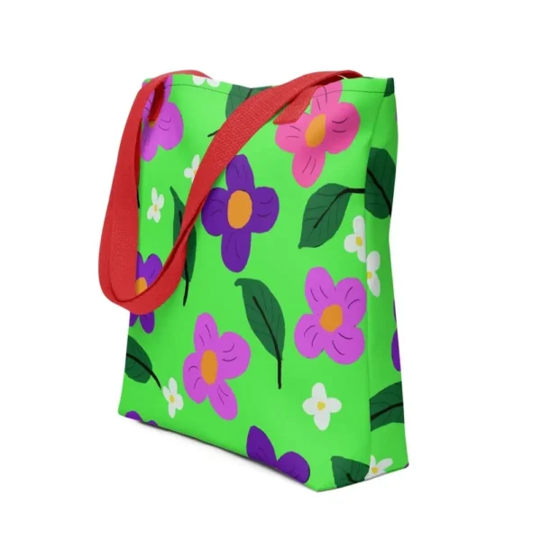 A green Spring all-over print tote bag with a vibrant flower and leaf design in pink, yellow, white and purple, set against a green background, featuring red handles