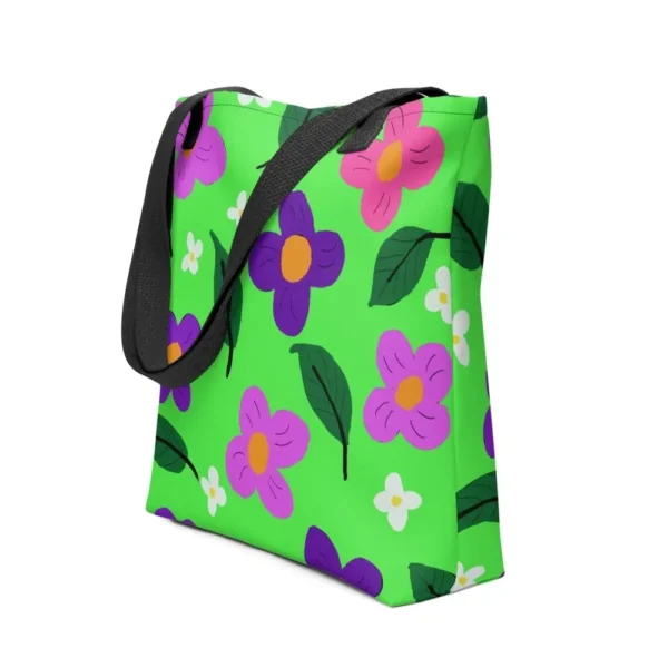 A green Spring all-over print tote bag with a vibrant flower and leaf design in pink, yellow, white and purple, set against a green background, featuring black handles