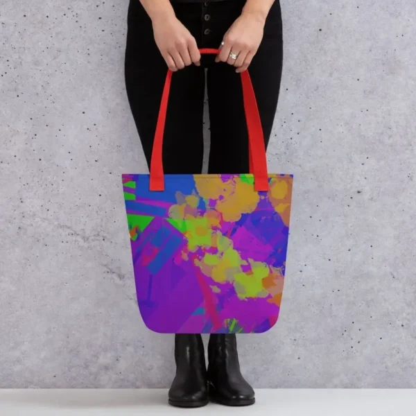 A person holding a Kaleidoscope Dream all-over print tote bag by the red handles, featuring a bold abstract pattern in green, purple, yellow, blue and pink, standing against a light speckled wall