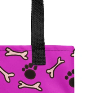 A Paul Corps large tote bag featuring a playful design of black paw prints and white bone motifs on a vibrant pink background, finished with sturdy black, red, yellow handles.