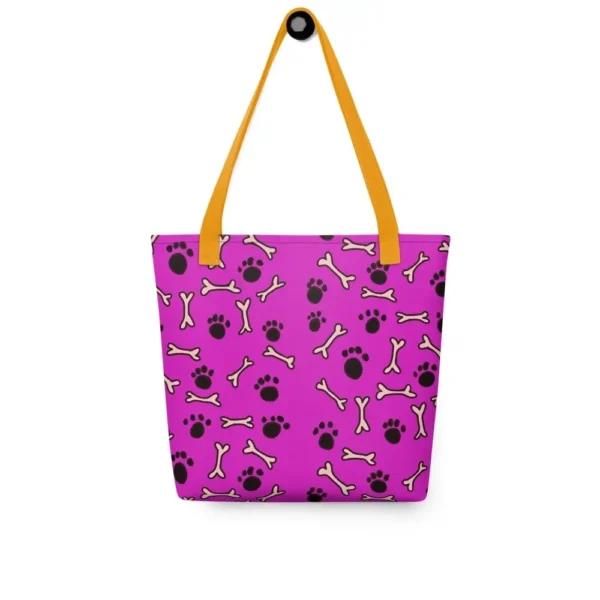 A Paul Corps large tote bag featuring a playful design of black paw prints and white bone motifs on a vibrant pink background, finished with sturdy black, red, yellow handles.