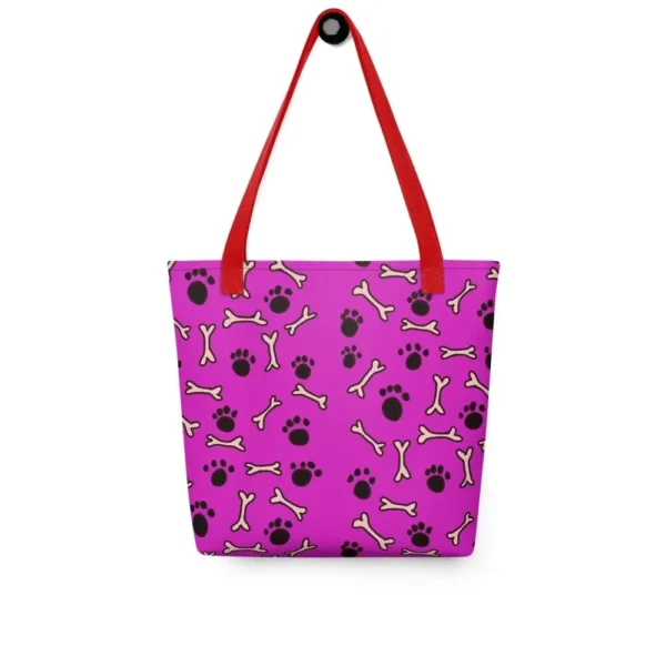 A Paul Corps large tote bag featuring a playful design of black paw prints and white bone motifs on a vibrant pink background, finished with sturdy black, red, yellow handles.