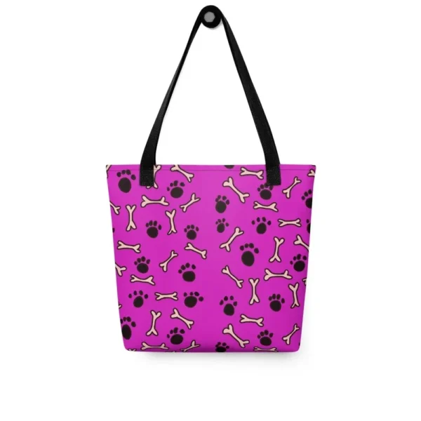 A Paul Corps large tote bag featuring a playful design of black paw prints and white bone motifs on a vibrant pink background, finished with sturdy black, red, yellow handles.