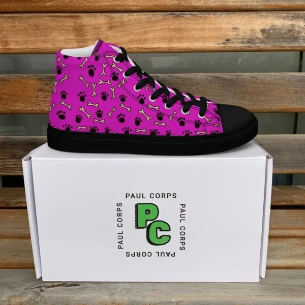 A pair of Paul Corps high-top canvas shoes with a vibrant pink background, decorated with black paw prints and white bone motifs, black laces, and black soles, displayed in front of a white Paul Corps branded box.