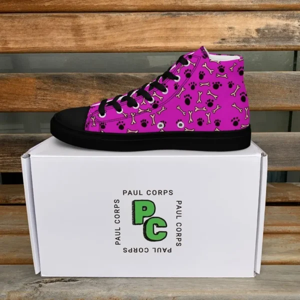 A pair of Paul Corps high-top canvas shoes with a vibrant pink background, decorated with black paw prints and white bone motifs, black laces, and black soles, displayed in front of a white Paul Corps branded box.