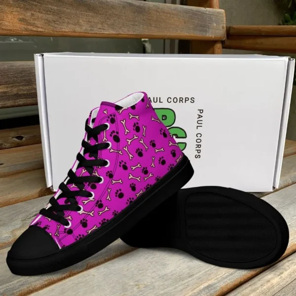 A pair of Paul Corps high-top canvas shoes with a vibrant pink background, decorated with black paw prints and white bone motifs, black laces, and black soles, displayed in front of a white Paul Corps branded box.