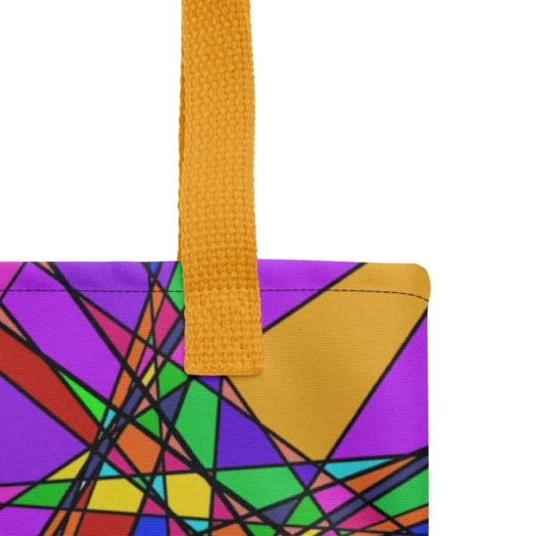 Close-up of the top corner of a Stain Glass Effect all-over print tote bag, showing the yellow handle and detailed stitching with the colourful abstract pattern in green, purple, yellow, and pink