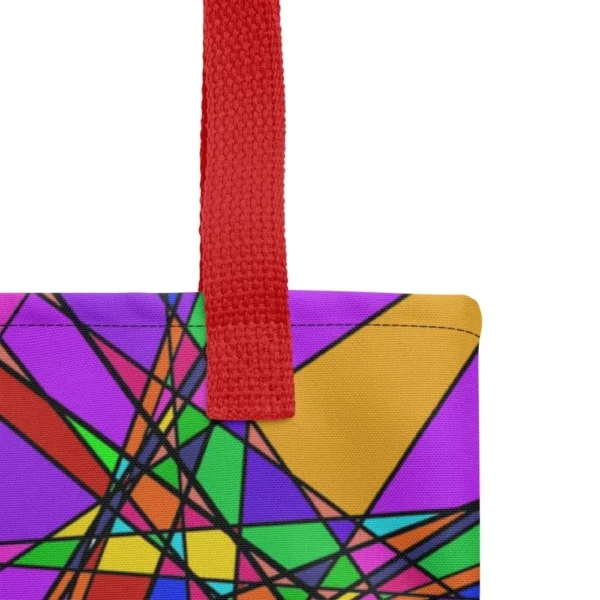 Close-up of the top corner of a Stain Glass Effect all-over print tote bag, showing the red handle and detailed stitching with the colourful abstract pattern in green, purple, yellow, and pink