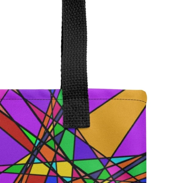 Close-up of the top corner of a Stain Glass Effect all-over print tote bag, showing the black handle and detailed stitching with the colourful abstract pattern in green, purple, yellow, and pink