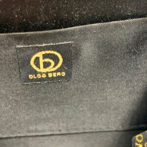 Olga Berg Classic Mini Top Handle Bag in black with original tag, style FC 6489, displayed on blue satin fabric.
