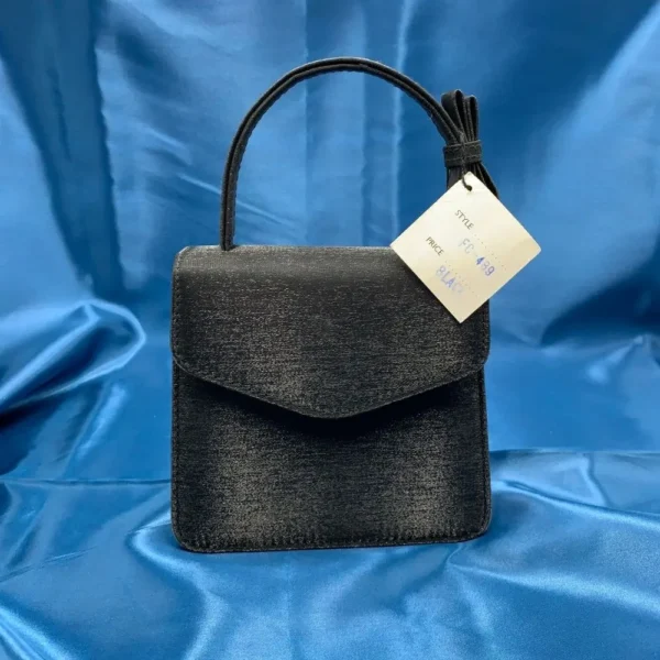 Olga Berg Classic Mini Top Handle Bag in black with original tag, style FC 6489, displayed on blue satin fabric.